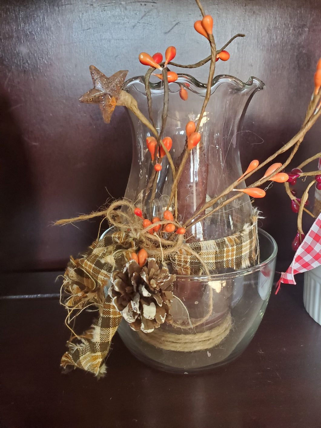 Candle holder with brown textured thin candle with orange berries, plaid ribbon and pine cone